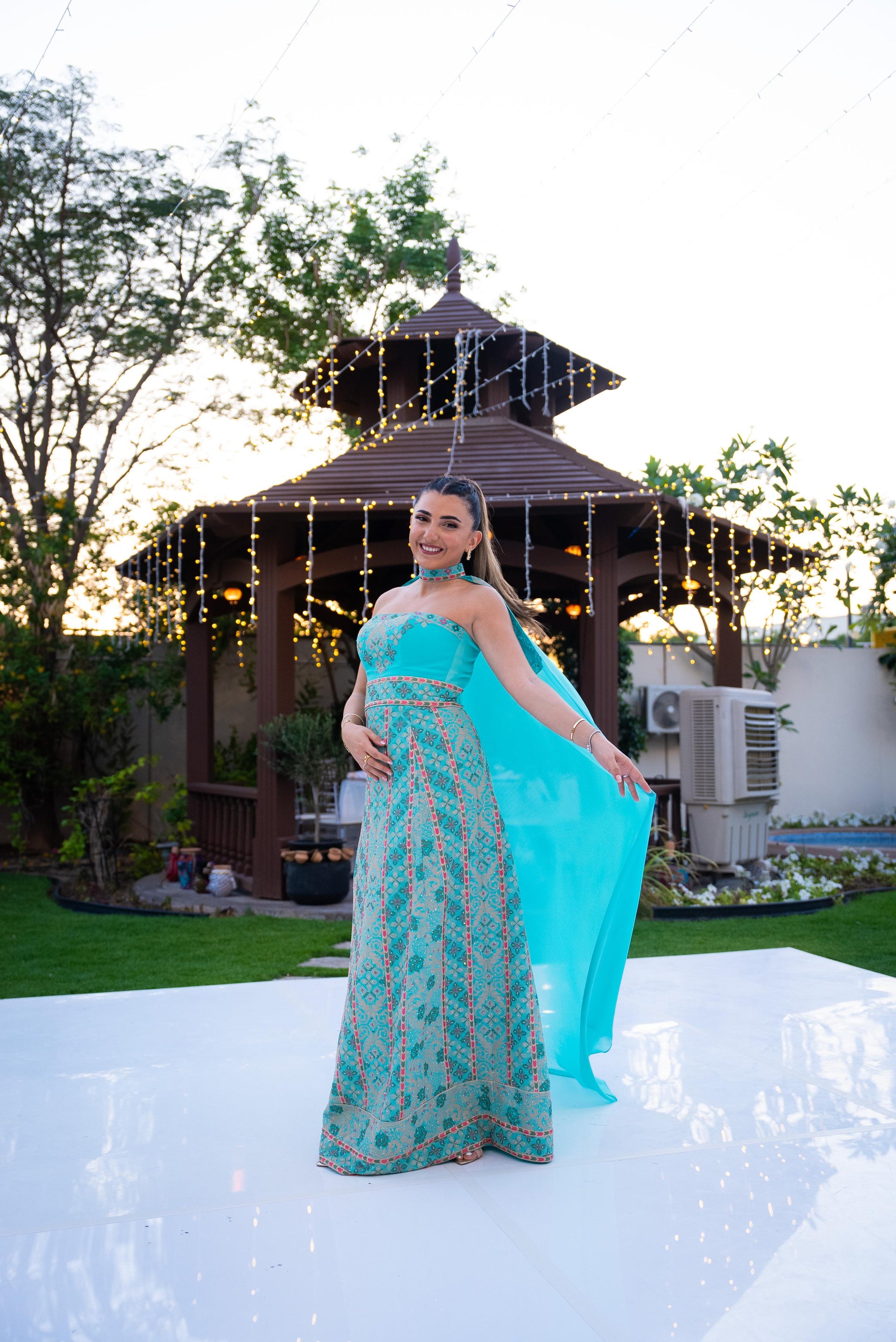 Woman in a palestinian blue henna dress standing in front of a gazebo with string lights